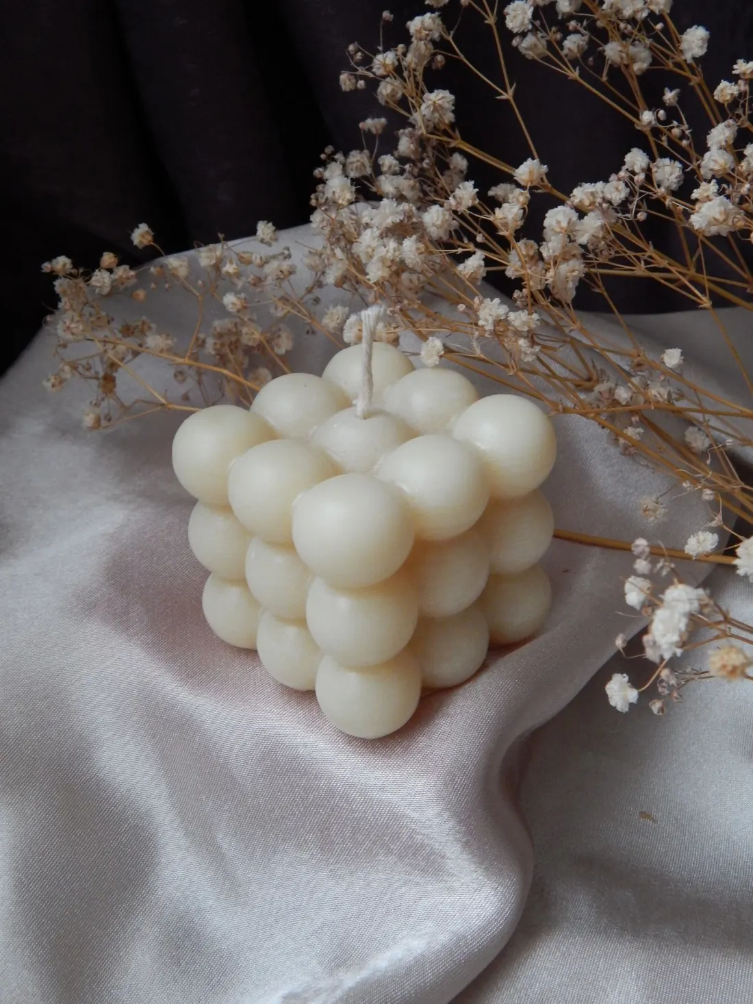 An ivory bubble candle on blush silk, styled with stems of dried baby's breath.