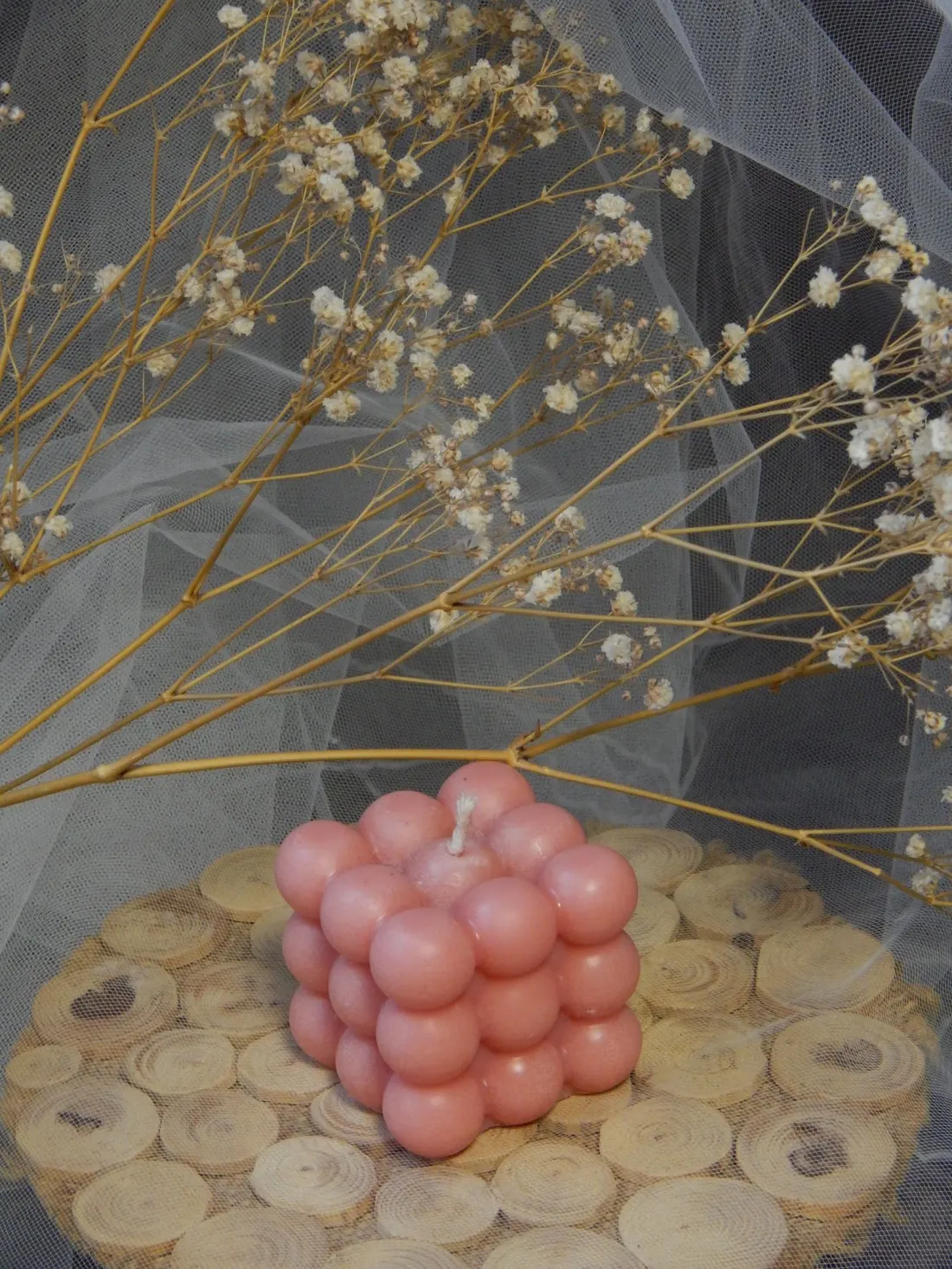 A blush pink bubble candle on a wooden coaster, with dried baby's breath behind it.